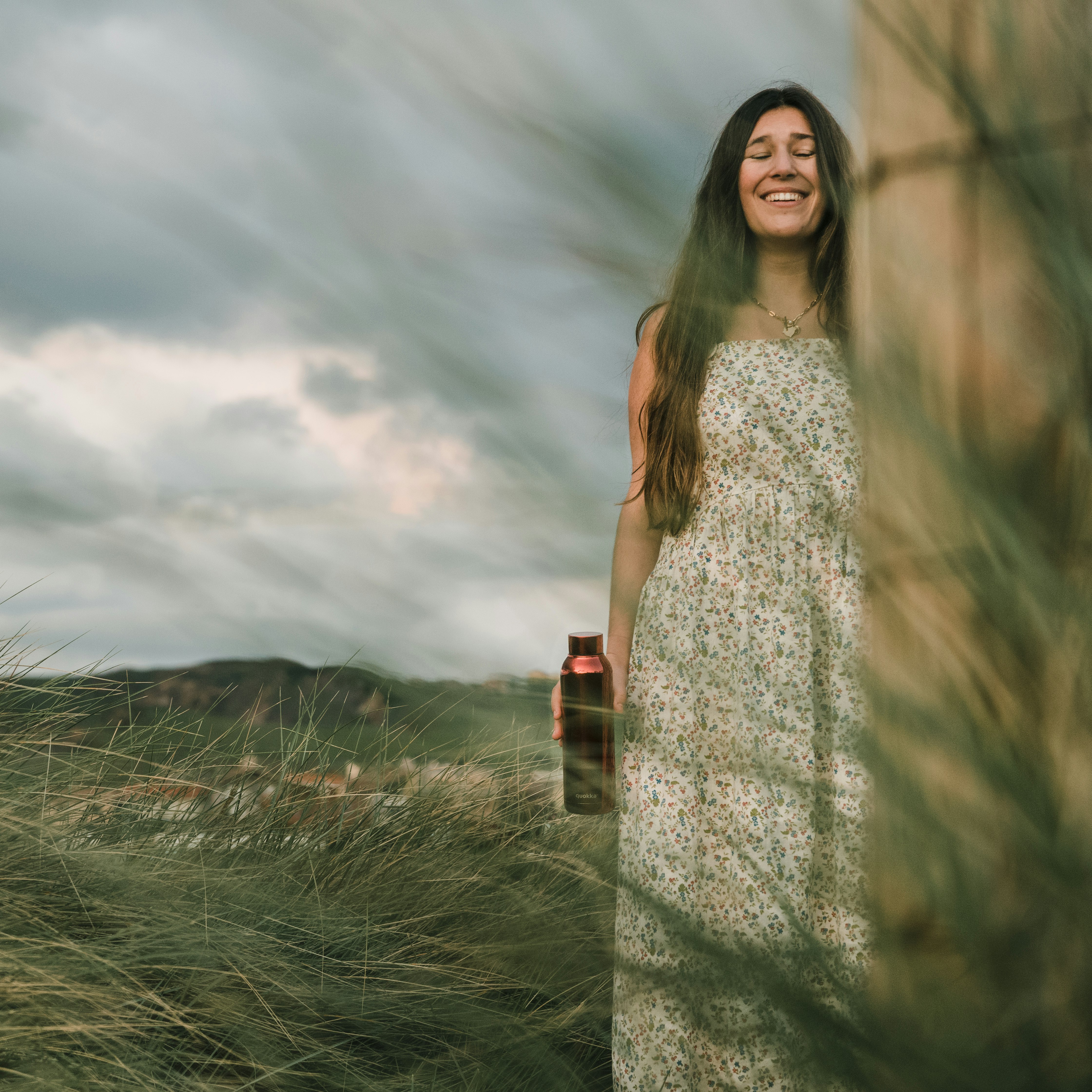 woman in white sleeveless dress standing on green grass field under white clouds during daytime